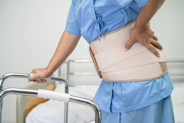 Asiatico signora paziente indossare mal di schiena supporto cintura per ortopedico lombare con walker. - Foto, immagini
