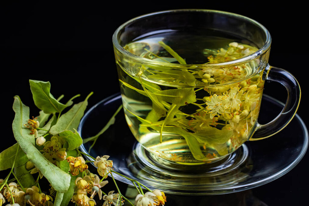 Cup of herbal tea with linden flowers on a black background. - Foto, Imagem