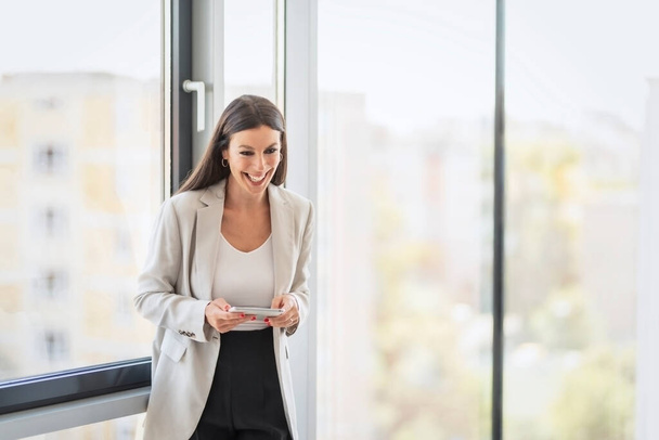 Portrait shot of happy businesswoman holding digital tablet in her hand while standing in a modern office.  - Valokuva, kuva