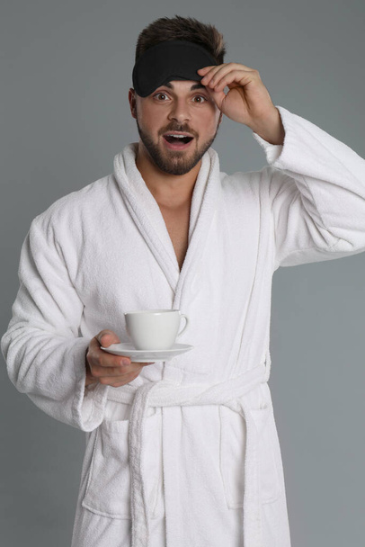 Young man in bathrobe with cup of coffee on grey background - Fotografie, Obrázek