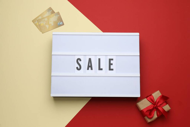 Lightbox with word Sale, gift box and credit cards on color background, flat lay - 写真・画像