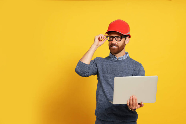 Professional engineer in hard hat with laptop on yellow background, space for text - Foto, immagini