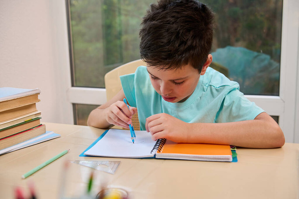 Handsome smart schoolboy using compass for drawing, draws circle while doing math and geometry homework. Back to school in new semester of the academic year. Online education concept. Homeschooling - Valokuva, kuva