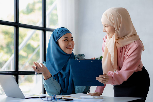 Two hijab-clad Asian women are brainstorming together in a conference room for a startup, run by a young, talented woman. The management concept runs the company of female leaders to grow the company. - Photo, Image