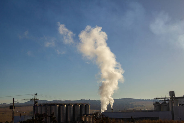 A factory emitting smoke into the environment, on a clear morning with the blue sky. - Foto, immagini