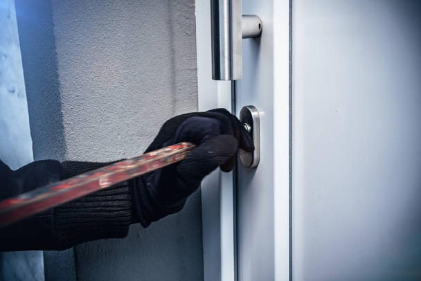 masked burglar with crowbar breaking and entering into a victim's home. motion blur selective focus - 写真・画像