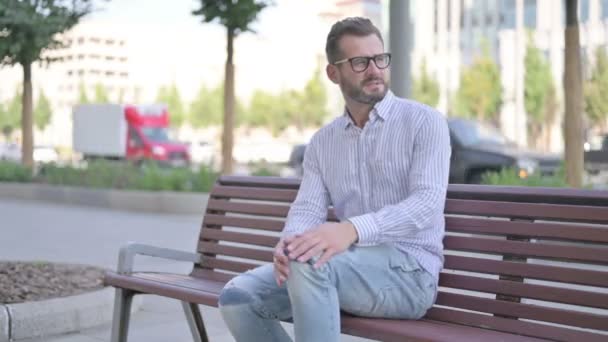Adult Man having Knee Pain while Sitting on Bench Outdoor - Video, Çekim