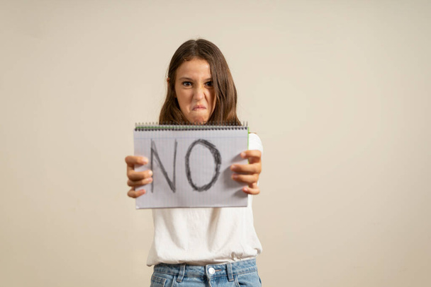 Latin teen girl over isolated beige background holding a sign with the text NO with sad expression - Foto, imagen
