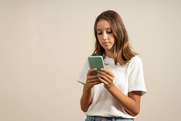 Pretty latin brunette teenager using mobile phone in casual clothes isolated on beige background - Φωτογραφία, εικόνα