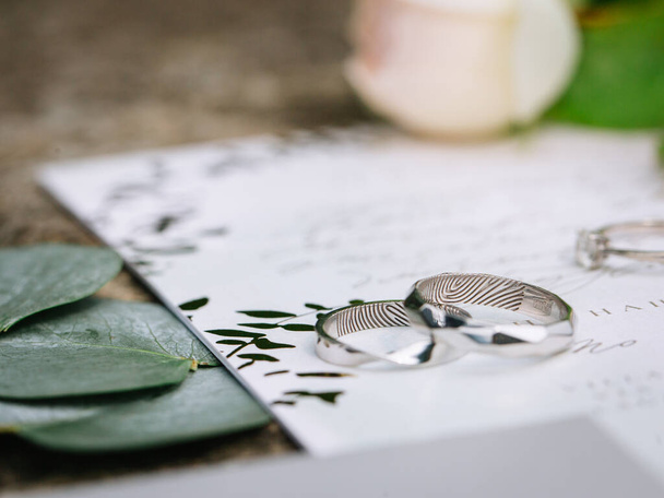 wedding silver engagement rings with fingerprint engraving inside. Lying on paper with calligraphy. nearby eucalyptus leaves - Foto, afbeelding