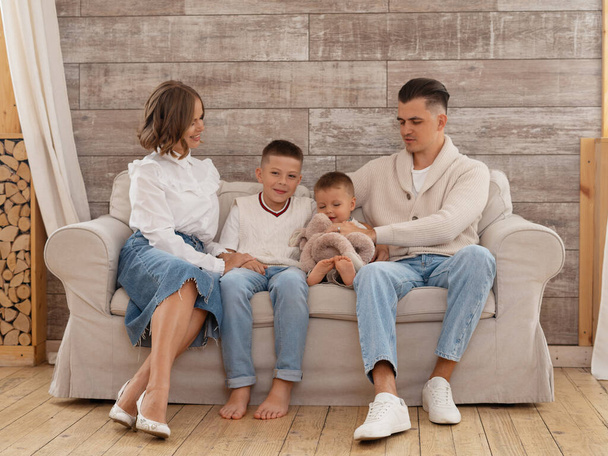 Family portrait. Happy parents with their two sons together, spend free time at home, being in good mood. Mother, father and small sons pose indoor. denim clothes - Foto, Imagem
