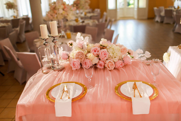 tafeldecoratie met roze tafelkleed, kristallen kandelaars met kaarsen en witte roze bloemen in restaurant. Stijlvolle trouwdag. Dektafel met gouden plaat, vork en mes. - Foto, afbeelding