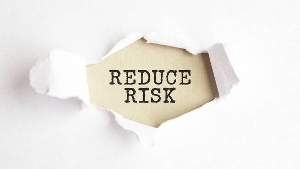 слово REDUCE Risk, що з'являється за рваним білим папером, сірий фон. - Фото, зображення