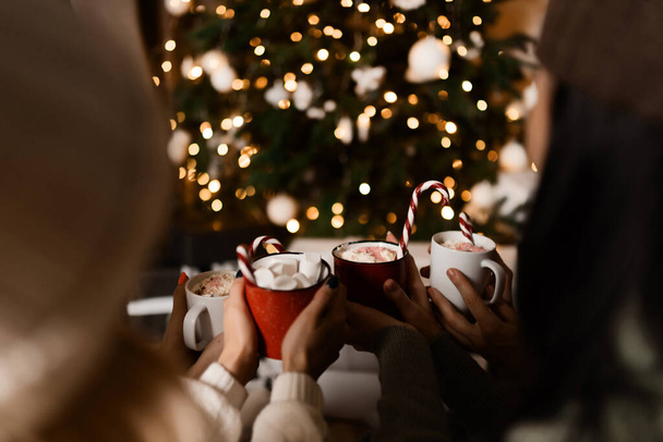 Woman holds a winter cup close up. Woman hands with elegant french manicure nails design holding a cozy knitted mug with cocoa, tea or coffee and a candy cane. Winter and Christmas time concept. - Foto, Imagem