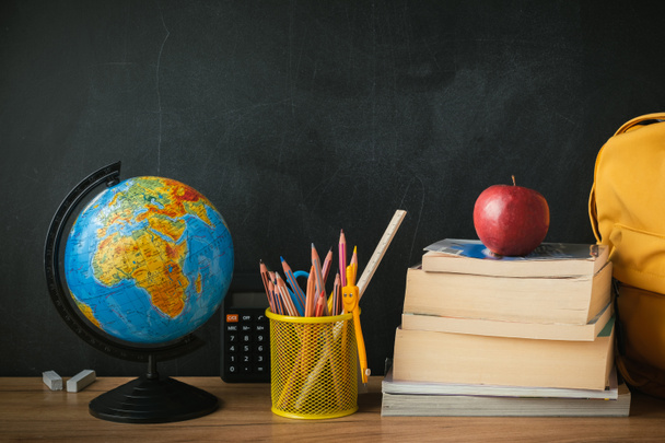 School supplies next to the globe and stack of books on the blackboard background. Back to school concept on September day - Foto, Imagem