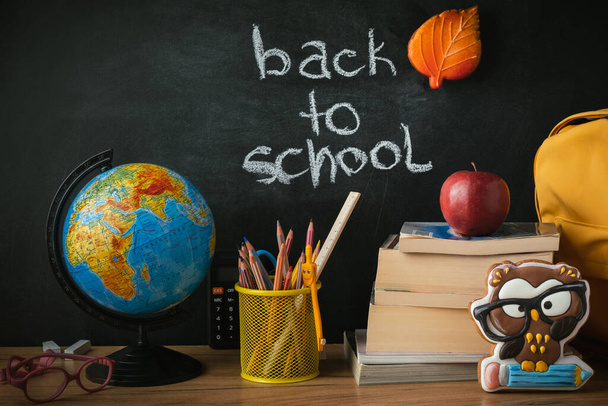 School supplies next to the globe and stack of books on the blackboard background. Back to school concept on September day - Foto, Imagen