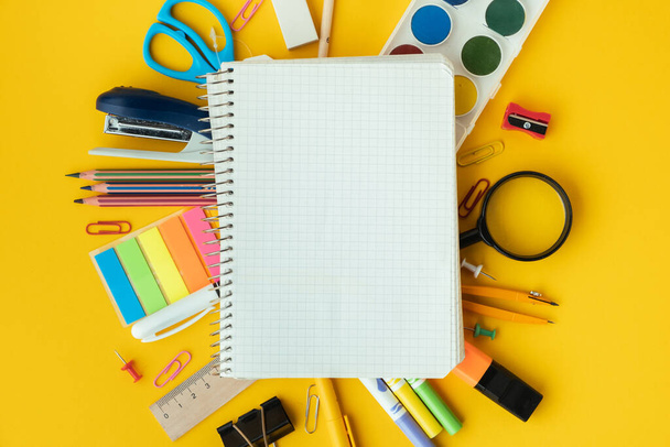 Blank notepad for free text next to the school supplies on the yellow background. Back to school concept on September day. Flat lay. Free space. - Fotó, kép