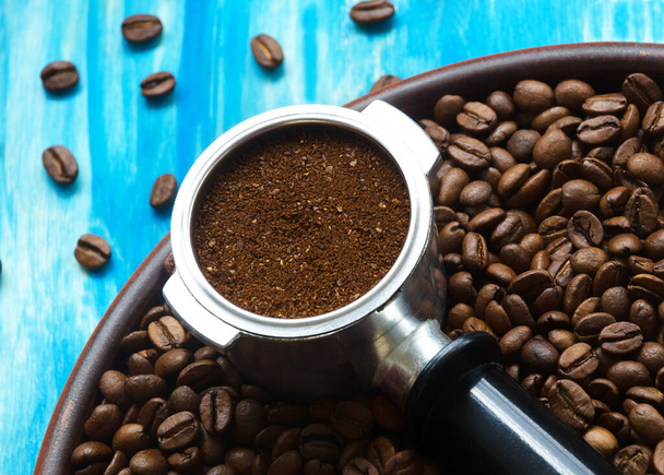 Кавовий конус і мелена кава лежать на кавових зернах і на керамічній тарілці. На бірюзовому тлі
. - Фото, зображення