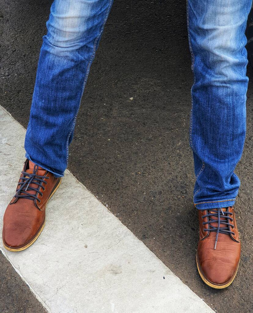 The lower of the legs of a standing man wearing blue denim jeans with brown leather shoes. - Fotoğraf, Görsel