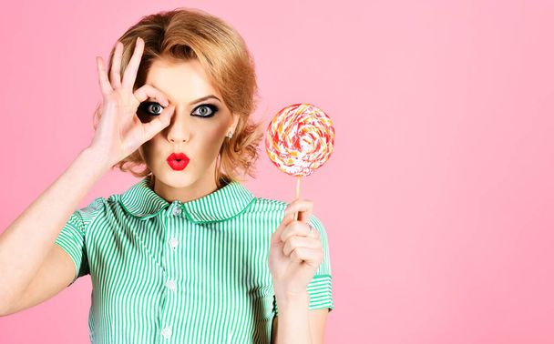 Beautiful girl with lollipop shows sign ok. Woman in summer style with colourful candy. Sweet food - Photo, Image