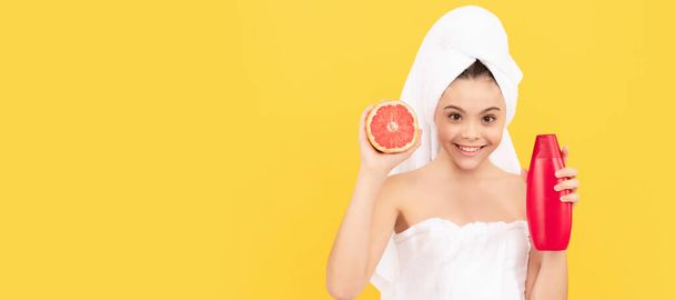 счастливый подросток в полотенце с бутылкой шампуня грейпфрута на желтом фоне. Косметика и уход за кожей для подростка, дизайн плакатов. Баннер с изображением девушки-красавицы - Фото, изображение