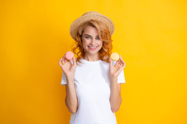Портрет молодой красивой женщины с миндалем. Французский макарон. Девушка наслаждается сладостями изолированы на желтом фоне - Фото, изображение