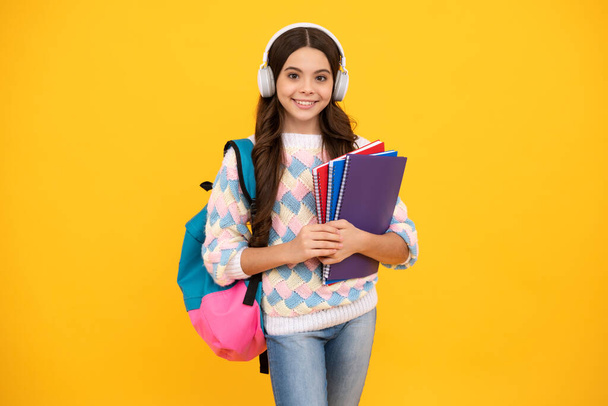 Back to school. Schoolgirl student in headphones with school bag backpack hold book on isolated studio background. School and education concept - Фото, зображення