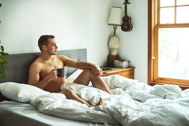 He loves starting the morning like this. a young handsome shirtless man drinking coffee and chilling in bed at home - Valokuva, kuva