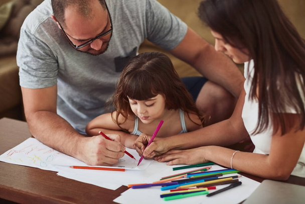 Οι δημιουργικές εκφράσεις είναι σημαντικές για την οικογένεια. μητέρα και πατέρας ζωγραφίζουν μαζί με τη μικρή τους κόρη στο σπίτι - Φωτογραφία, εικόνα