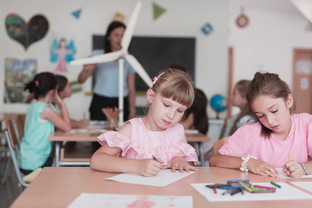 Little girls sitting in elementary school drawing on paper with their friends while sitting in a modern classroom. High quality photo - Photo, Image
