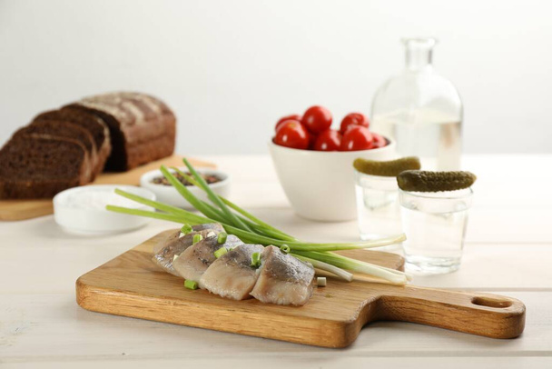 Wooden board with delicious salted herring slices and green onion on white table - Zdjęcie, obraz