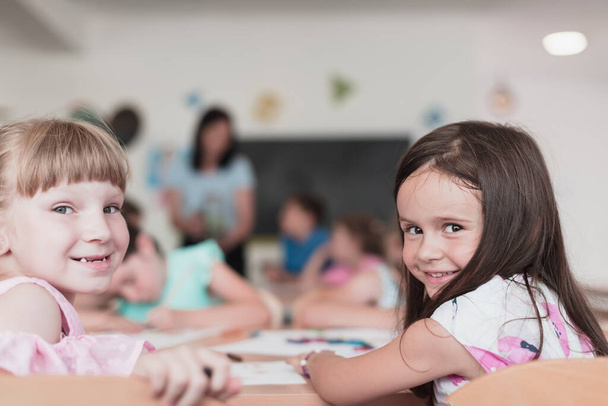Little girls sitting in elementary school drawing on paper with their friends while sitting in a modern classroom. High quality photo - Foto, Bild