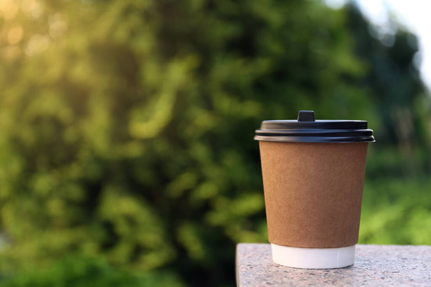 Disposable paper cup with plastic lid on stone parapet outdoors, space for text - Foto, afbeelding
