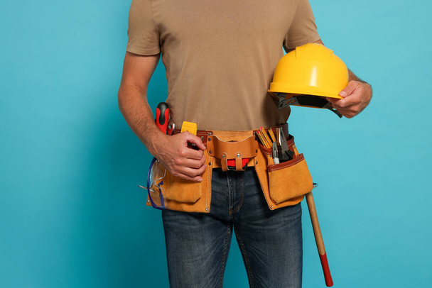 Professional builder with hard hat and tool belt on light blue background, closeup - Foto, imagen