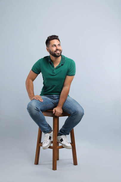 Handsome young man sitting on stool against light grey background - 写真・画像