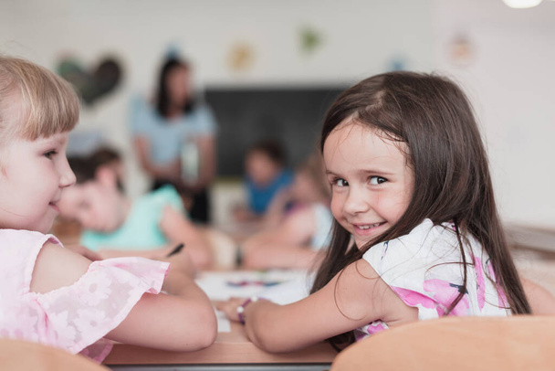 Little girls sitting in elementary school drawing on paper with their friends while sitting in a modern classroom. High quality photo - Fotografie, Obrázek