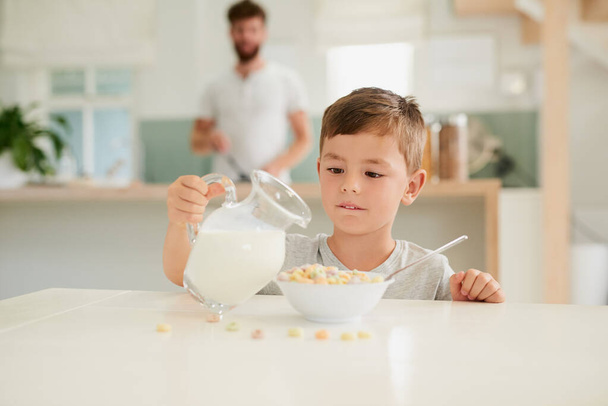 Растущие мальчики должны есть. очаровательный маленький мальчик завтракает со своим отцом на заднем плане дома - Фото, изображение