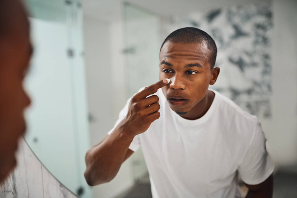 Upping his skincare game. a handsome young man applying moisturizer to his face in the bathroom at home - Foto, imagen
