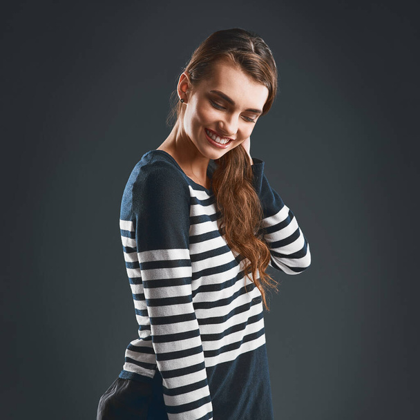 Nothing stops her from smiling. Studio shot of a cheerful young woman holding her neck while standing against a dark background - Foto, immagini