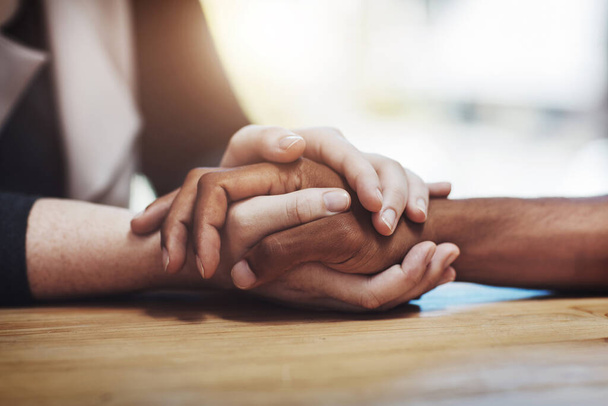Support, compassion and trust while holding hands and sitting together at a table. Closeup of a loving, caring and interracial couple or friends comforting each other after a loss or cancer news. - Fotografie, Obrázek