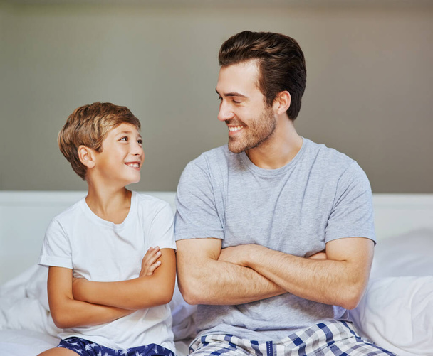 Following in his fathers footsteps. a cheerful father and son seated on a bed with arms folded while looking at the camera at home in the morning - 写真・画像