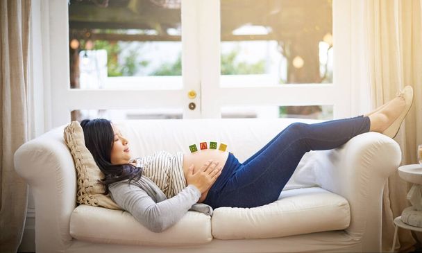 Relaxing for two. an attractive young pregnant woman balancing wooden blocks on her tummy while relaxing on the sofa at home - Foto, Imagem