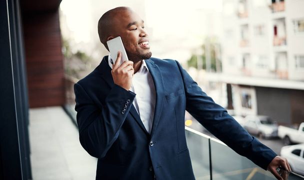 Keeping his career right on track. a handsome young businessman talking on a cellphone outside his office - Foto, imagen