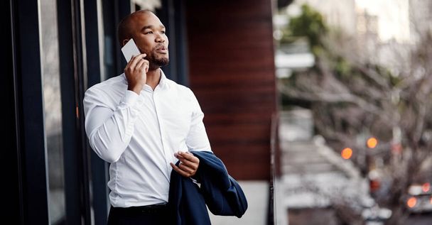 He works hard to keep every client happy. a handsome young businessman talking on a cellphone outside his office - Foto, imagen