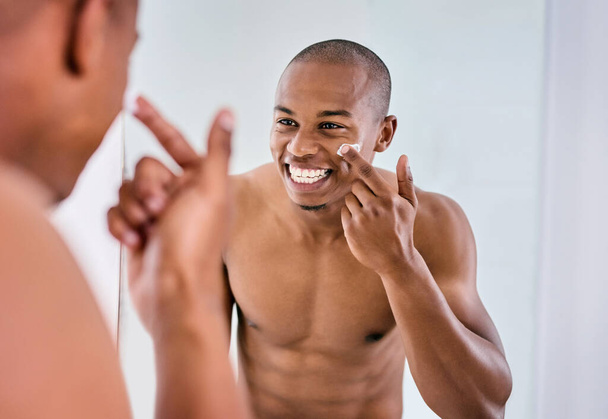 Візьми його на шкіру. красивий молодий чоловік наносить зволожуючий крем на обличчя у ванній вдома
 - Фото, зображення