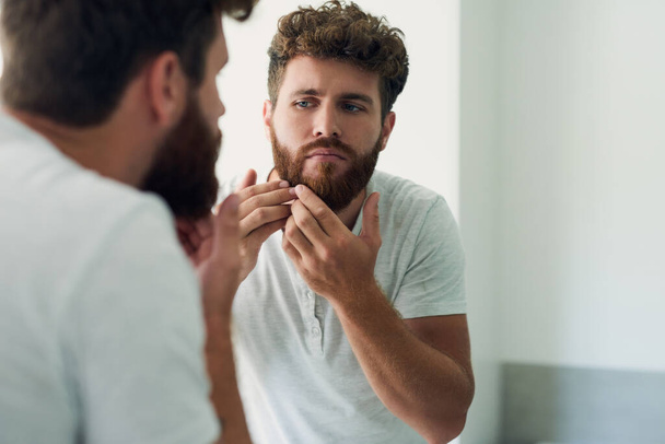 Checking your skin for any blemishes is important. a handsome young man checking out his skin in the bathroom mirror - Foto, afbeelding