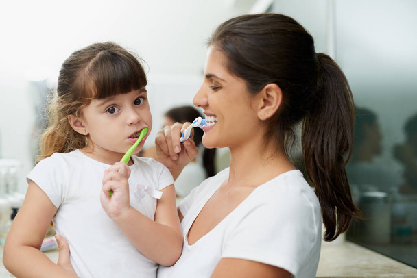 This is the way we brush our teeth. Portrait of a mother and daughter brushing their teeth together in the bathroom at home - Fotoğraf, Görsel