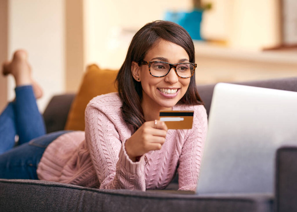 Settled in for a virtual shopping spree. an attractive young woman using a laptop and credit card on the sofa at home - 写真・画像