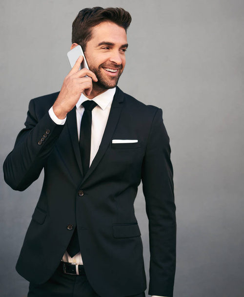 Он всегда готов ответить на твой звонок. Студийный снимок красивого молодого бизнесмена, использующего мобильный телефон на сером фоне - Фото, изображение