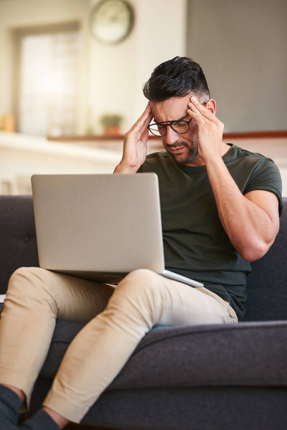 Я не могу справиться с этой мигренью. красивый молодой человек, страдающий головной болью во время работы над ноутбуком дома - Фото, изображение